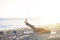 Senior woman exercising, stretching on yoga mat at the beach, doing leg raises