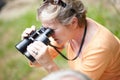 Senior, woman and binocular in forest for travel, sightseeing or vacation and scenery in nature. Elderly, lady or person