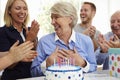 Senior Woman Blows Out Birthday Cake Candles At Family Party