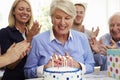 Senior Woman Blows Out Birthday Cake Candles At Family Party