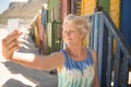 Senior woman clicking selfie while standing against beach hut Royalty Free Stock Photo