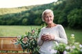 Senior woman with coffee standing outdoors on a terrace in summer.