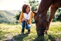 A senior woman crouching and a horse grazing by a stable. Royalty Free Stock Photo