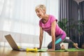 Senior woman doing stretching exercises in front of laptop at home, watching online tutorials