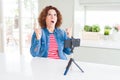 Senior woman doing video chat using smartphone camera amazed and surprised looking up and pointing with fingers and raised arms Royalty Free Stock Photo