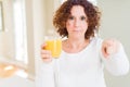 Senior woman driking a glass of fresh orange juice pointing with finger to the camera and to you, hand sign, positive and Royalty Free Stock Photo