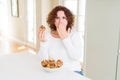 Senior woman eating chocolate chips muffins cover mouth with hand shocked with shame for mistake, expression of fear, scared in Royalty Free Stock Photo
