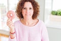 Senior woman eating pink sugar donut with a confident expression on smart face thinking serious Royalty Free Stock Photo