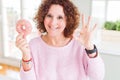 Senior woman eating pink sugar donut doing ok sign with fingers, excellent symbol Royalty Free Stock Photo