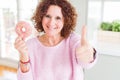 Senior woman eating pink sugar donut happy with big smile doing ok sign, thumb up with fingers, excellent sign Royalty Free Stock Photo