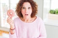 Senior woman eating pink sugar donut scared in shock with a surprise face, afraid and excited with fear expression Royalty Free Stock Photo