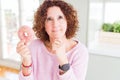 Senior woman eating pink sugar donut serious face thinking about question, very confused idea Royalty Free Stock Photo