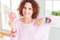 Senior woman eating pink sugar donut with surprise face pointing finger to himself Royalty Free Stock Photo