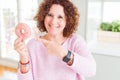 Senior woman eating pink sugar donut very happy pointing with hand and finger Royalty Free Stock Photo