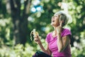 Woman exercising in park while listening to music. Mature woman eat banana resting after exercise Royalty Free Stock Photo