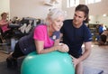 Senior Woman Exercising On Swiss Ball Being Encouraged By Personal Trainer In Gym Royalty Free Stock Photo