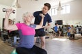 Senior Woman Exercising On Swiss Ball With Weights Being Encouraged By Personal Trainer In Gym Royalty Free Stock Photo