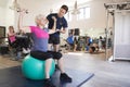 Senior Woman Exercising On Swiss Ball With Weights Being Encouraged By Personal Trainer In Gym Royalty Free Stock Photo