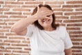 Senior woman with glasses standing over bricks wall smiling and laughing with hand on face covering eyes for surprise Royalty Free Stock Photo