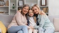 A senior woman grandmother, a young mother and a small granddaughter are sitting on the sofa, hugging, happy to meet