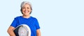 Senior woman with gray hair holding weight machine to balance weight loss looking positive and happy standing and smiling with a