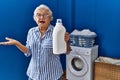 Senior woman with grey hair holding detergent bottle celebrating achievement with happy smile and winner expression with raised Royalty Free Stock Photo