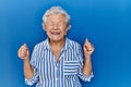 Senior woman with grey hair standing over blue background excited for success with arms raised and eyes closed celebrating victory Royalty Free Stock Photo