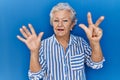 Senior woman with grey hair standing over blue background showing and pointing up with fingers number eight while smiling Royalty Free Stock Photo