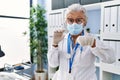 Senior woman with grey hair wearing doctor uniform and medical mask holding syringe pointing finger to one self smiling happy and Royalty Free Stock Photo