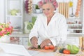 Portrait of senior woman in hair rollers cutting vegetables on kitchen table Royalty Free Stock Photo