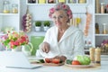 Portrait of senior woman in hair rollers cutting vegetables on kitchen table Royalty Free Stock Photo