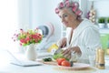 Senior woman in hair rollers cutting vegetables on kitchen table Royalty Free Stock Photo