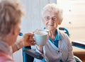 Senior woman, happy friends and toast coffee in wheelchair in room, house or nursing home together. Elderly women, mug Royalty Free Stock Photo