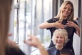 Senior Woman Having Hair Cut By Female Stylist In Hairdressing Salon