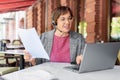 Senior woman with headset is filling forms whie sitting in front of laptop monitor at summer cafe. Royalty Free Stock Photo