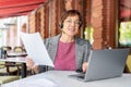 Senior woman in headset working in front of laptop monitor. She looking at camera and smiling while sitting in summer Royalty Free Stock Photo