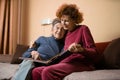 Senior woman and her adult daughter looking at photo album together on couch in living room, talking joyful discussing memories. Royalty Free Stock Photo