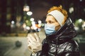 Senior woman holding coffee to go, wearing protective medical mask and white latex gloves, walk outdoors at night, observing Royalty Free Stock Photo