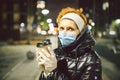 Senior woman holding coffee to go, wearing protective medical mask and white latex gloves, walk outdoors at night, observing Royalty Free Stock Photo