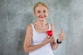 Senior woman holding red heart toy and show Thumbs up  in fitness gym. aged lady exercising.  Old female workout .Mature sport Royalty Free Stock Photo