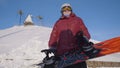 Senior woman holding snowboard. Bottom view happy senior woman in helmet and glasses, wearing ski suit, standing in