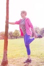 Active Senior woman holding tree trunk while doing leg exercise in park Royalty Free Stock Photo