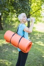 Senior woman holds fitness mat on her back in the park and preparing for exercise Royalty Free Stock Photo