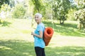 Senior woman holds fitness mat on her back in the park and preparing for exercise Royalty Free Stock Photo