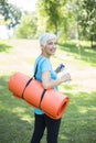 Senior woman holds fitness mat on her back in the park and preparing for exercise Royalty Free Stock Photo