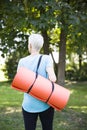 Senior woman holds fitness mat on her back in the park Royalty Free Stock Photo