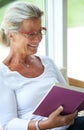 Senior woman, home and book with smile for reading, relax and living room with ideas for story, knowledge or glasses