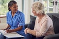 Senior Woman At Home Talking To Female Nurse Or Care Worker In Uniform Making Notes In Folder Royalty Free Stock Photo