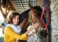 A senior woman with a horse standing by a stable. Royalty Free Stock Photo