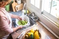 A senior woman in the kitchen washing the broccoli. Some tropical fruit close to her. Healthy eating